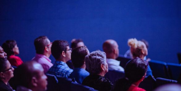 An attentive group of adults seated at an indoor conference, focusing on a presentation.